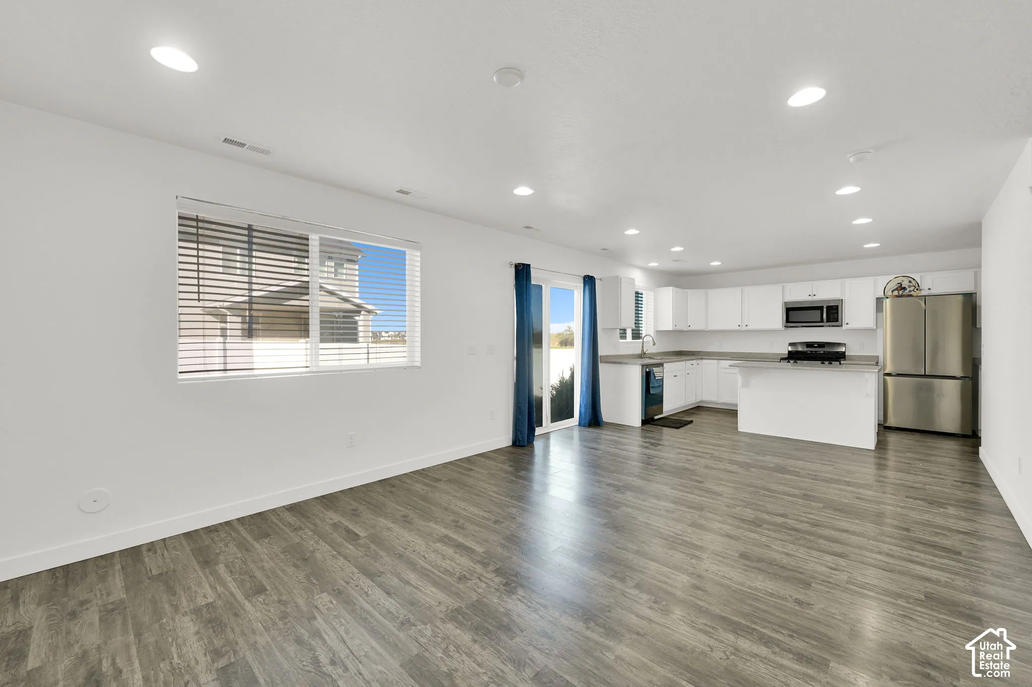 Open-concept interior featuring wood-finish flooring, recessed lighting, white cabinetry, stainless steel appliances, and sliding glass patio doors