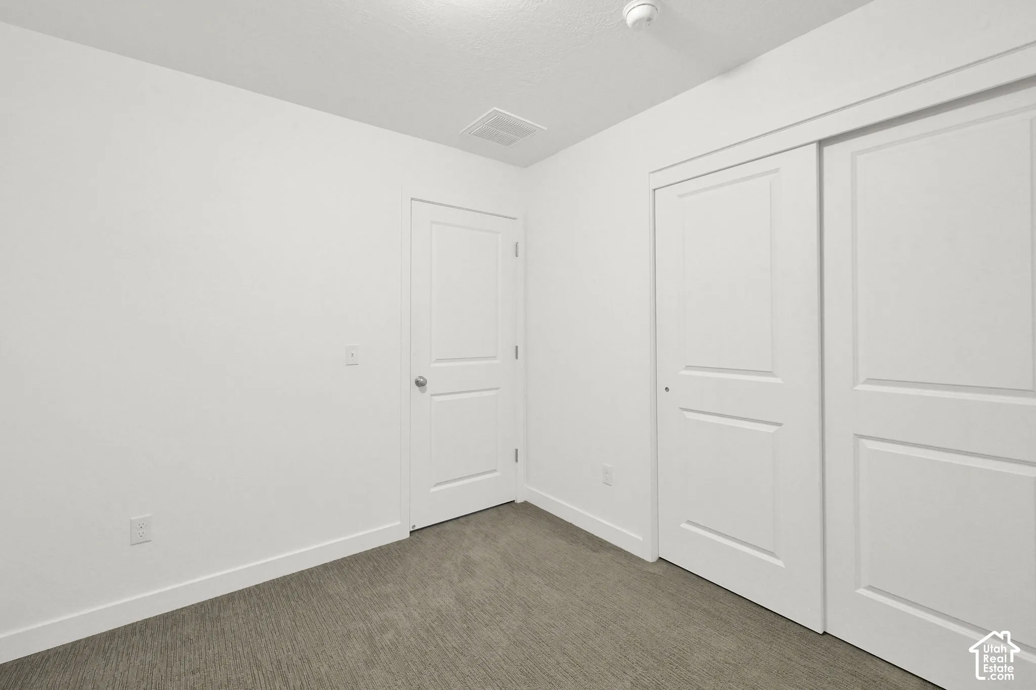 Room featuring neutral-toned carpeting, two-panel interior doors, and sliding closet doors