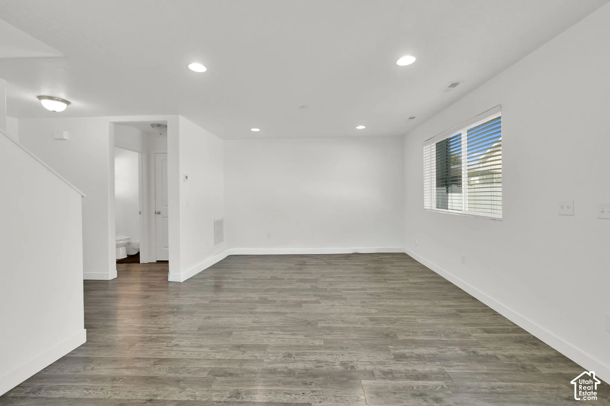 Neutral-toned interior space featuring wood-finish flooring, recessed lighting, and a window with horizontal blinds