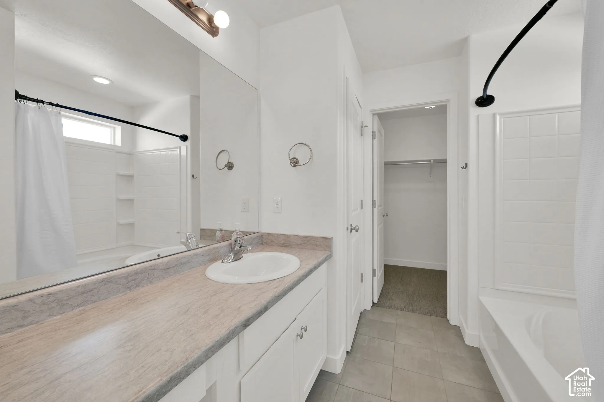 Full-width vanity with solid-surface countertop and integrated sink, large wall-mounted mirror, ceramic tile flooring, and combination tub and shower enclosure
