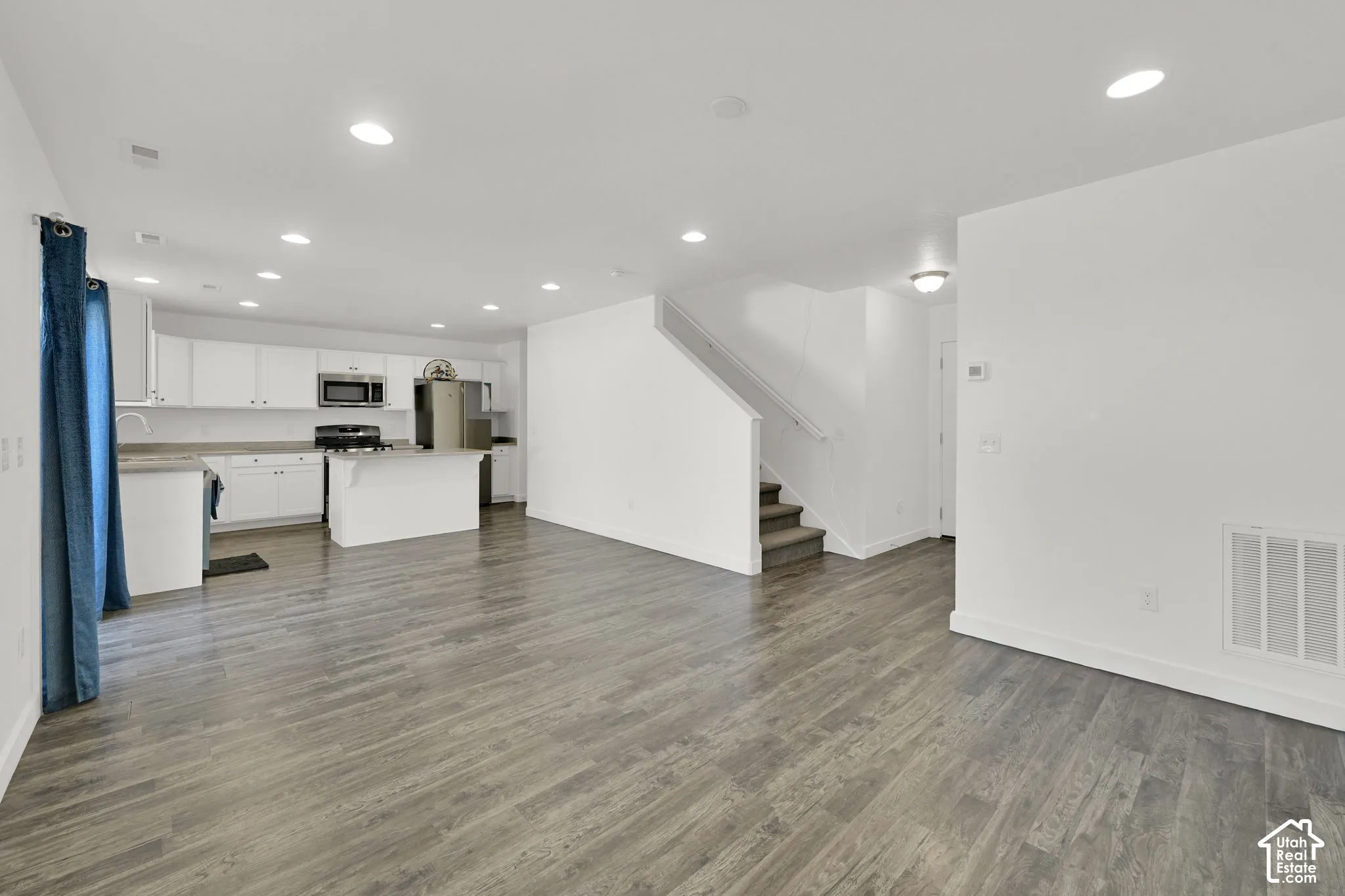 Open-concept interior featuring wood-finish flooring, recessed lighting, white cabinetry, a kitchen peninsula, and a staircase with a handrail