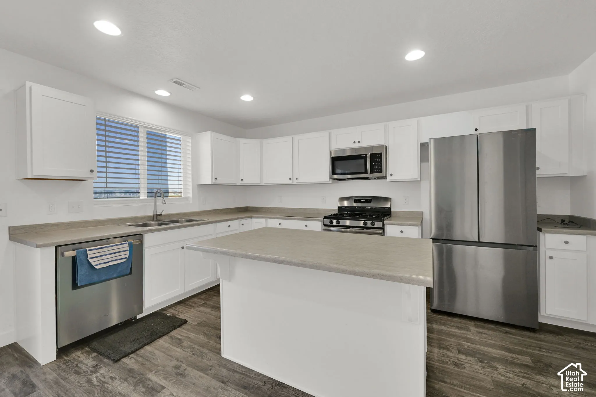 Kitchen featuring white shaker-style cabinetry, a central island, neutral solid-surface countertops, wood-finish flooring, and stainless steel appliances
