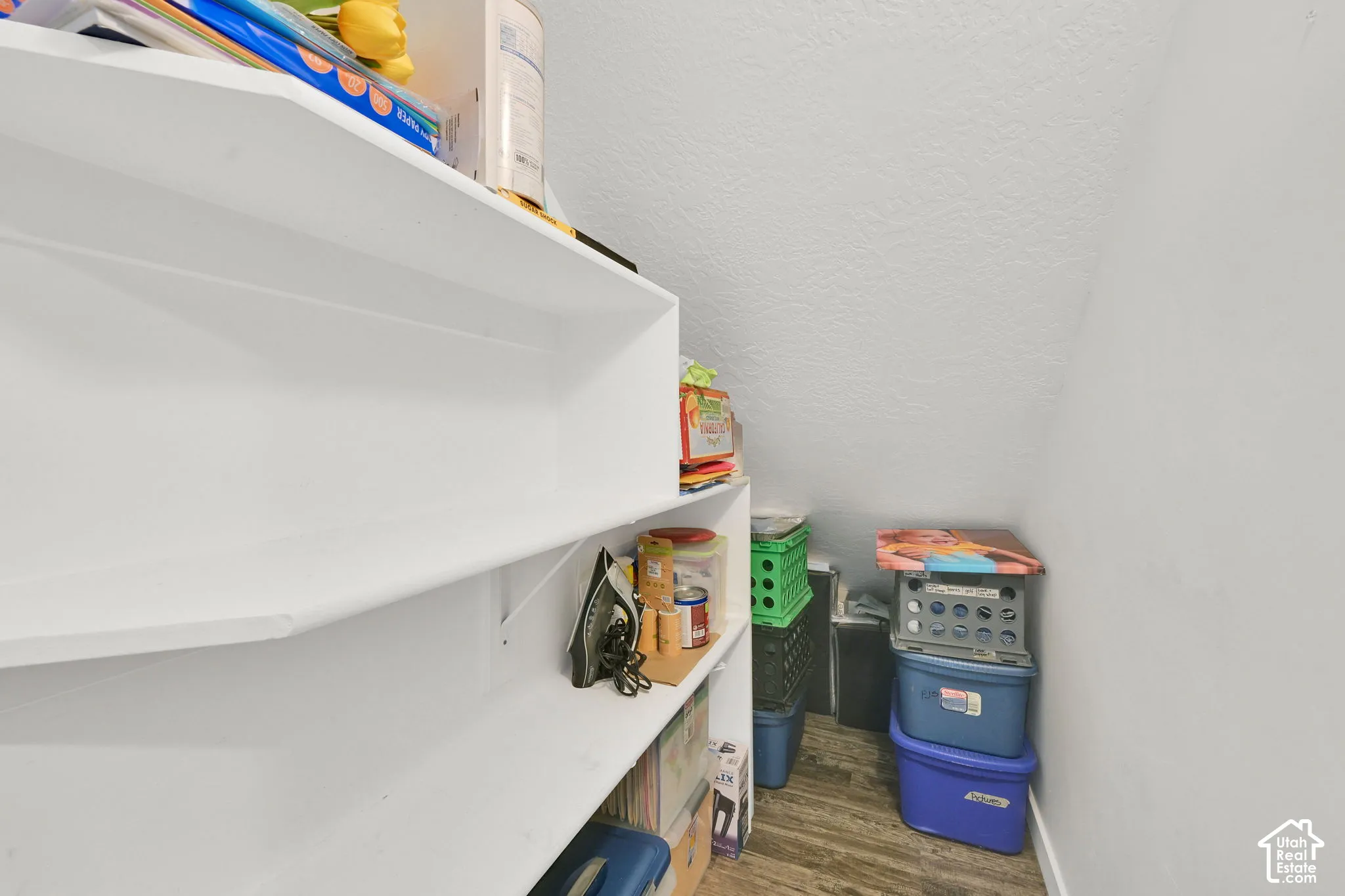 Storage area featuring white built-in shelving and wood-finish flooring