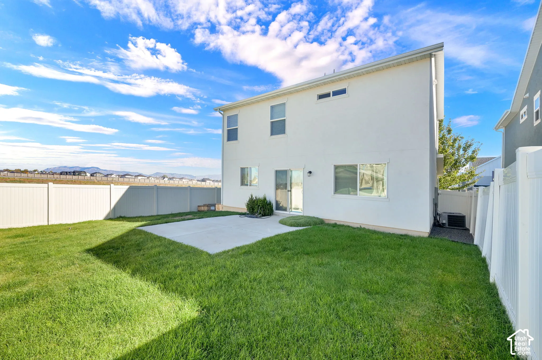 Rear exterior featuring a concrete patio, manicured lawn, and full-height vinyl fencing