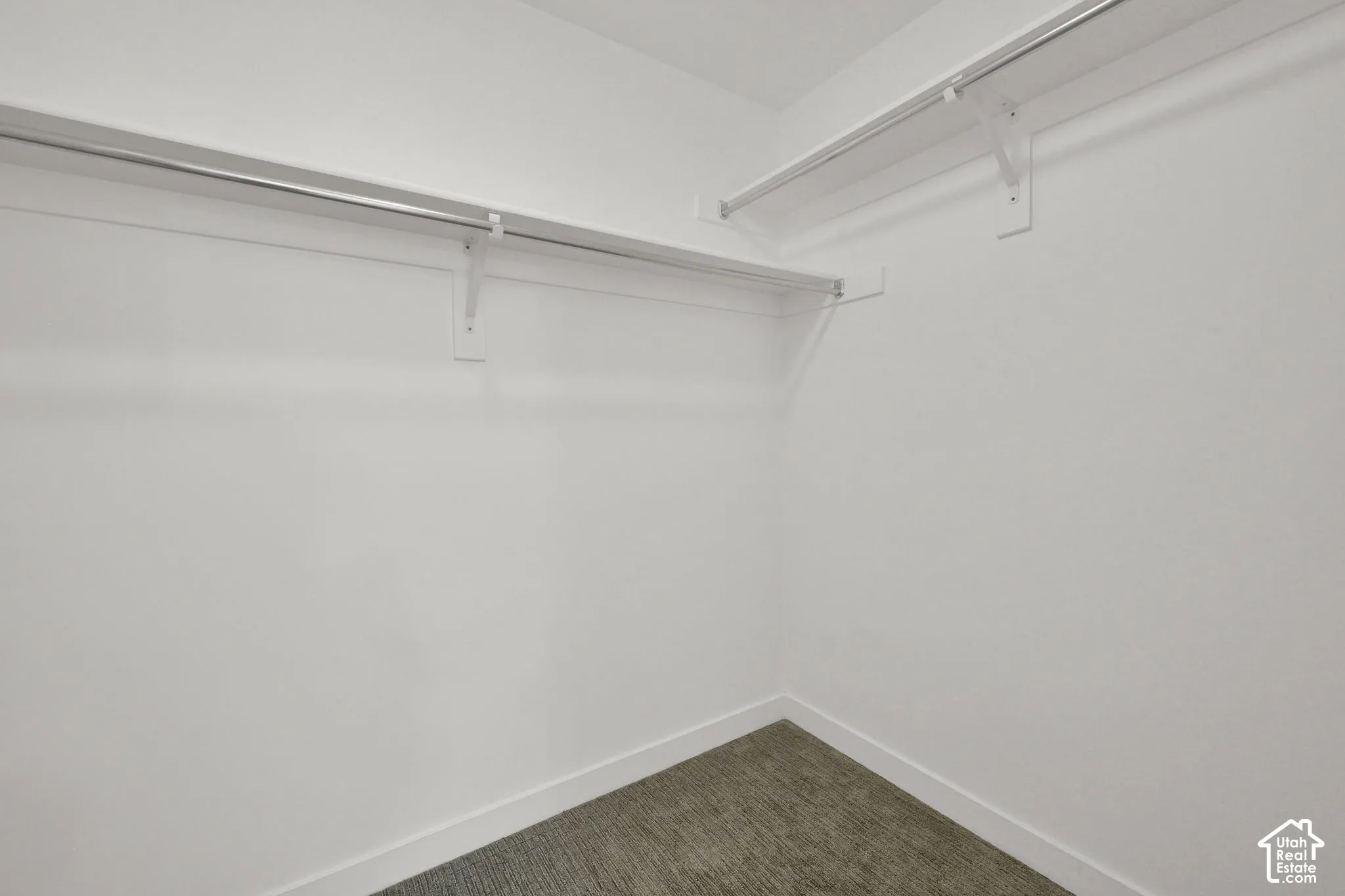 Storage space featuring neutral wall-to-wall carpeting and tiered, white-finish built-in shelving with integrated hanging rods