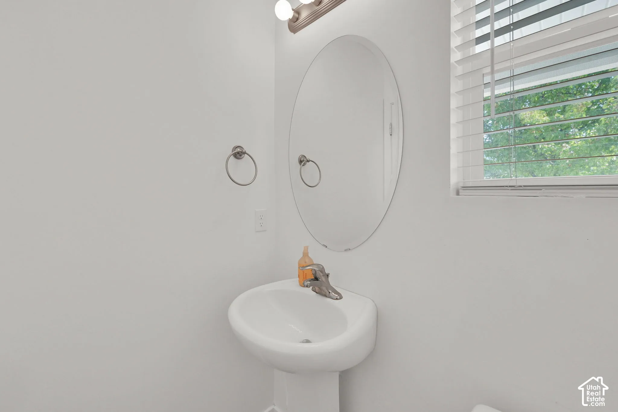 Wall-mounted oval mirror, white pedestal sink with metal faucet, and multi-light vanity fixture