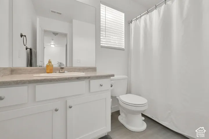 Bathroom featuring a white vanity with integrated oval sink, stone-finish countertop, large wall-mounted mirror, and combination shower and tub with horizontal slat blinds