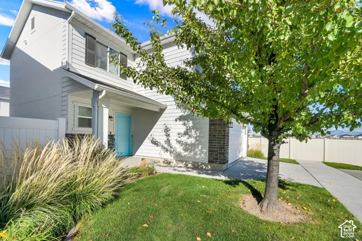 Two-story residence featuring horizontal lap siding, stone veneer accents, an attached two-car garage, concrete driveway, and a front lawn with mature landscaping