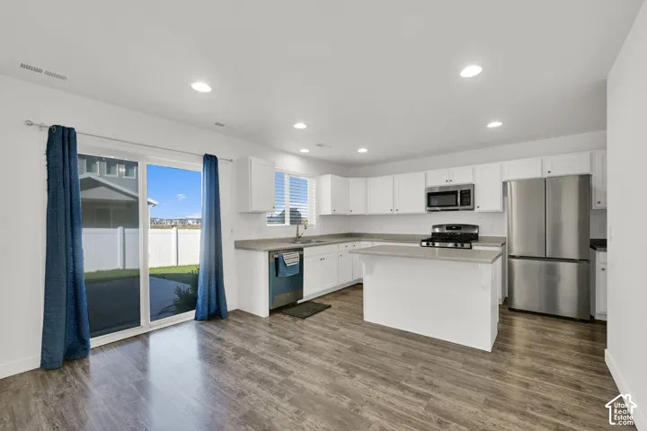 Kitchen featuring white cabinetry, an island with countertop surface, stainless steel appliances, recessed lighting, and wood-finish flooring