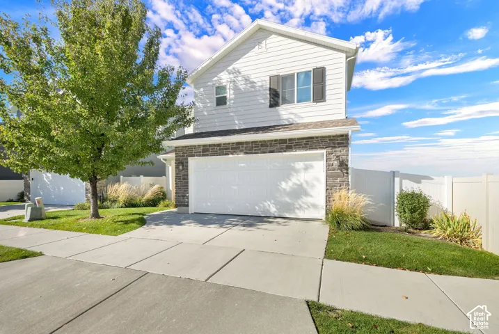 Two-story exterior featuring white horizontal siding, stone veneer accents, a double-car garage, and a white privacy fence