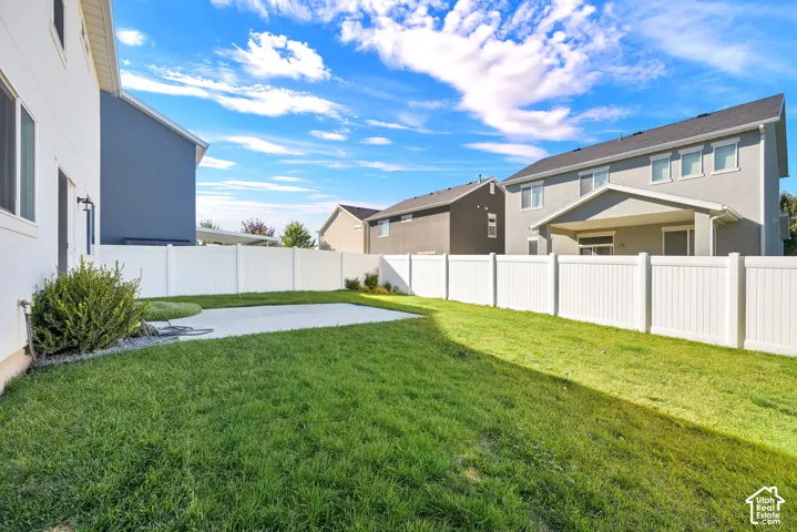 Backyard featuring a manicured lawn, concrete patio, and white vinyl perimeter fencing