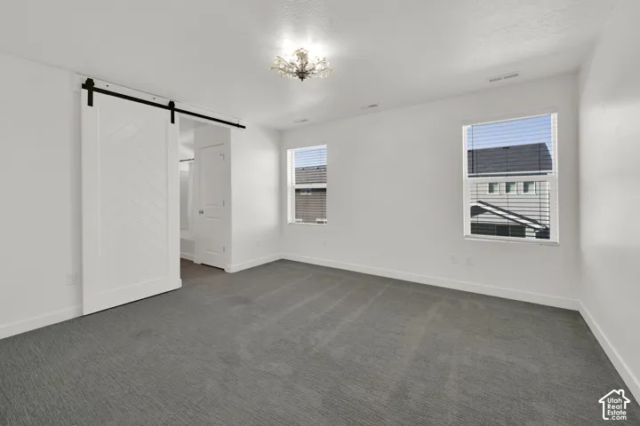 Room featuring herringbone-patterned sliding barn door, wall-to-wall carpeting, decorative flush-mount ceiling fixture, and dual windows