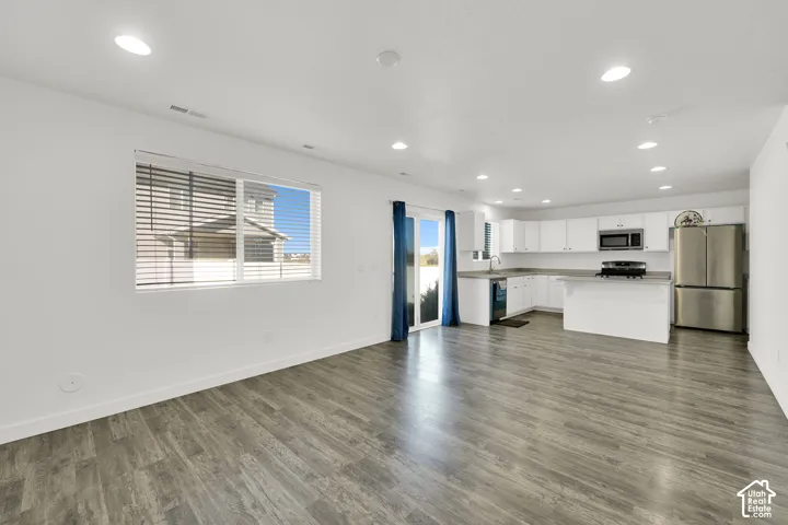 Open-concept interior featuring wood-finish flooring, recessed lighting, white cabinetry, stainless steel appliances, and sliding glass patio doors