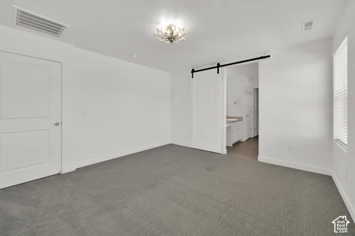 Interior space featuring gray carpeted flooring, a white sliding barn door on a matte black track, a multi-bulb flush-mount light fixture, and a white panel door