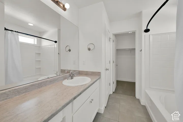 Full-width vanity with solid-surface countertop and integrated sink, large wall-mounted mirror, ceramic tile flooring, and combination tub and shower enclosure