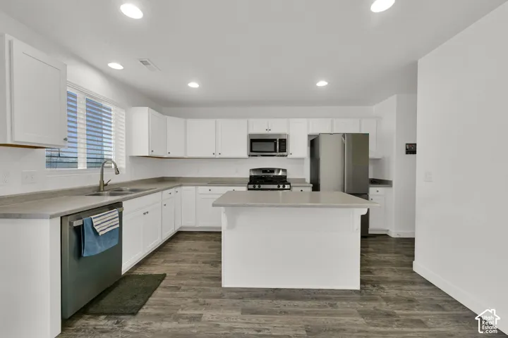 Kitchen featuring white cabinetry, solid surface countertops, stainless steel appliances, a central island, and wood-finish flooring