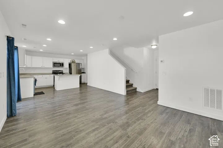 Open-concept interior featuring wood-finish flooring, recessed lighting, white cabinetry, a kitchen peninsula, and a staircase with a handrail