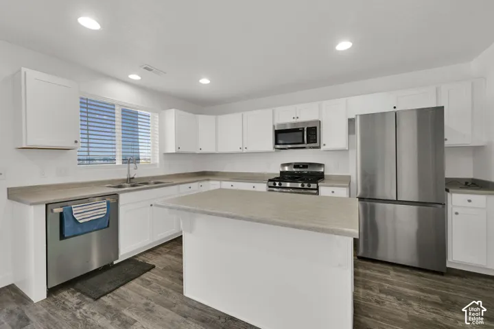 Kitchen featuring white shaker-style cabinetry, a central island, neutral solid-surface countertops, wood-finish flooring, and stainless steel appliances