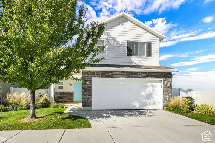 Two-story exterior featuring horizontal siding, stone veneer accents, a double-car garage, and a contrast-color front door