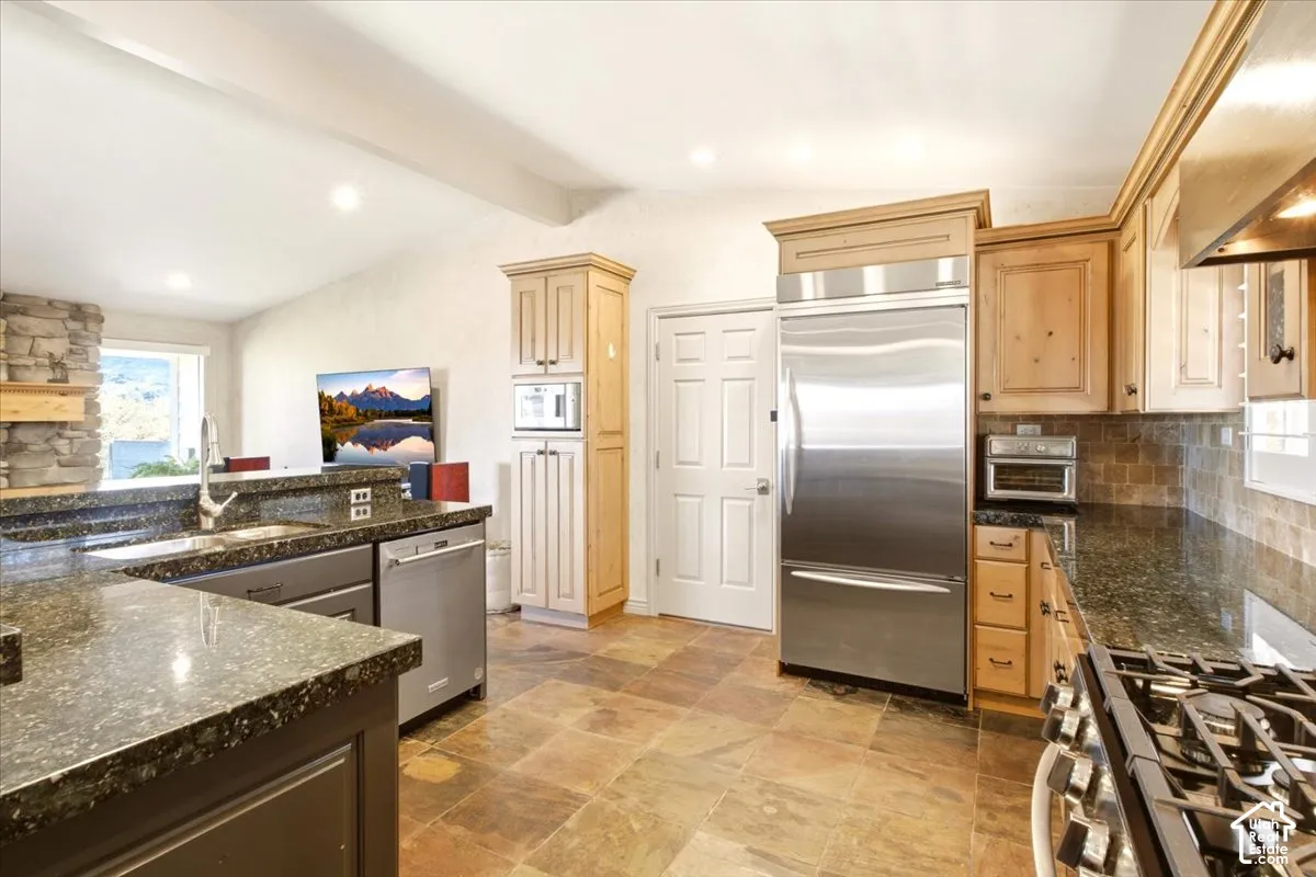 Kitchen featuring stone-finish countertops, stainless steel appliances, natural-finish wood cabinetry, stone-style tile flooring, and a stone-clad hearth