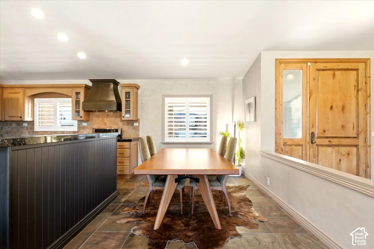 Kitchen featuring wood cabinetry, dark metal range hood, stone-finish countertops, tile flooring, and custom wood-paneled entry door with glass pane
