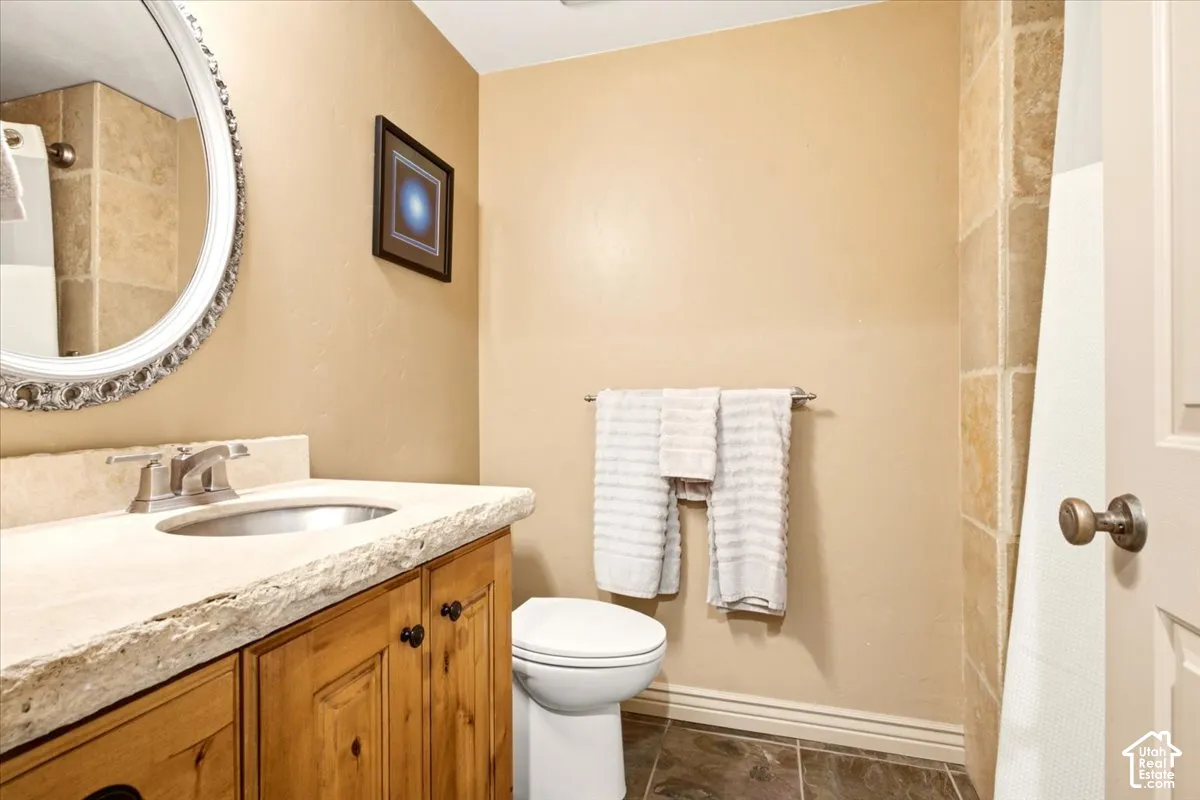 Bathroom featuring a wooden vanity with a natural-edge stone countertop, undermount sink, circular decorative mirror, and stone-tiled shower surround