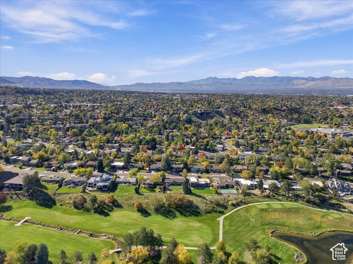 Aerial perspective of an expansive neighborhood featuring mature tree canopy, integrated golf course fairways, a water feature, and distant mountain backdrops