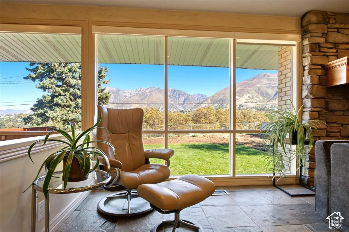 Floor-to-ceiling windows, natural stone fireplace surround, tile flooring, and mountain backdrop