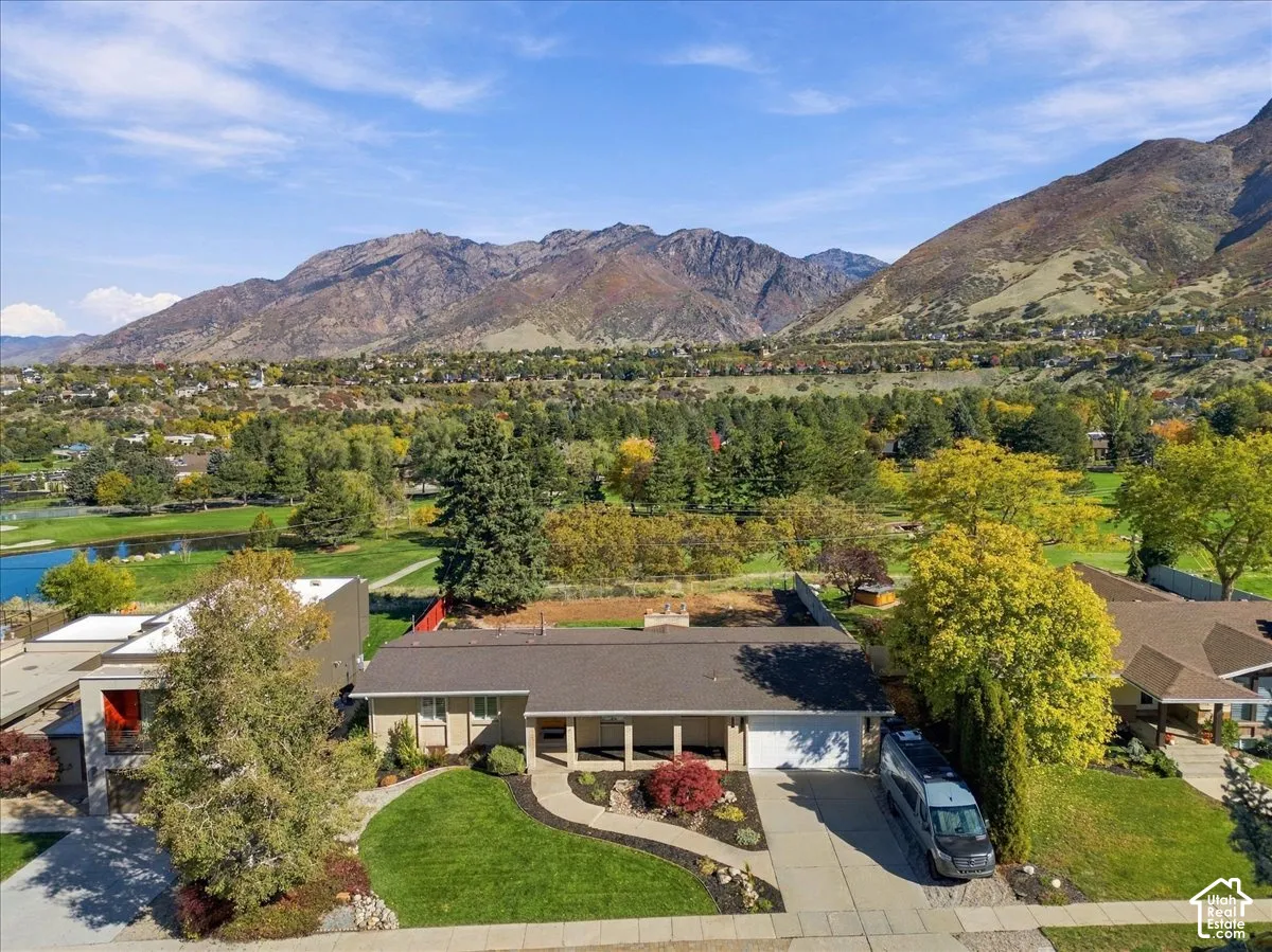 Single-level residence with a concrete driveway, attached garage, covered front porch, and manicured landscaping, set against a mountainous backdrop
