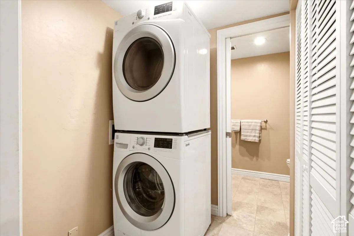 Stacked white front-load laundry unit, louvered bi-fold closet doors, and ceramic tile flooring