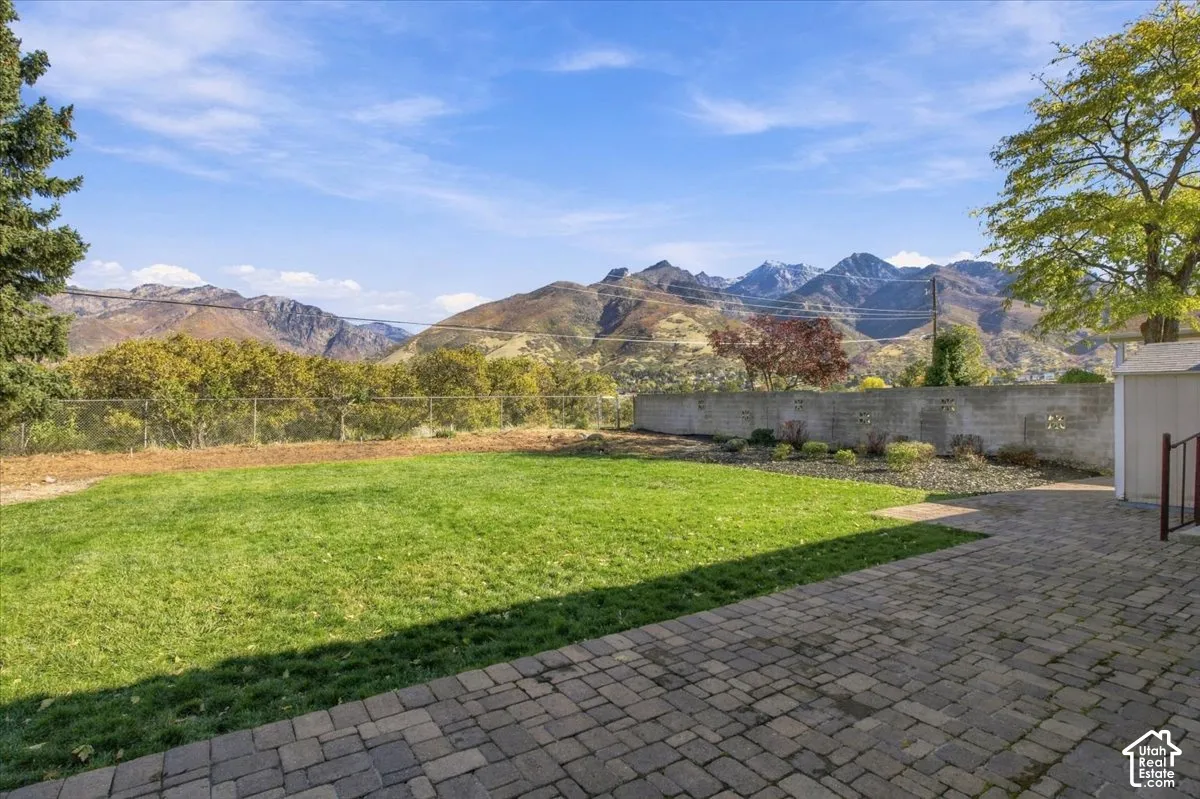 Backyard featuring a paver stone patio, level lawn, concrete block perimeter wall, and mountain backdrop
