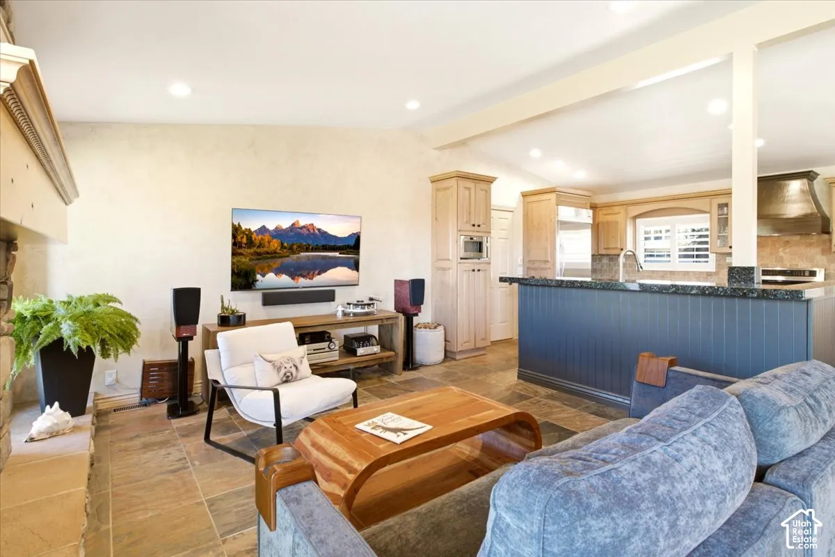 Open-concept interior featuring stone-tile flooring, recessed lighting, a stone fireplace, and a kitchen island with a dark-finished panel base and stone countertop