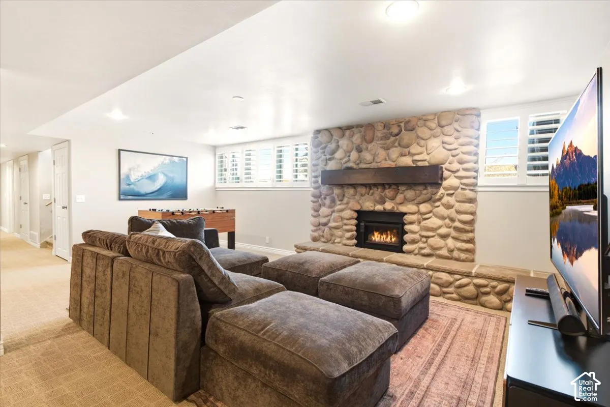 Floor-to-ceiling river rock fireplace with a built-in firebox, elevated stone hearth, and heavy timber mantel, complemented by recessed lighting and shutter-style window coverings
