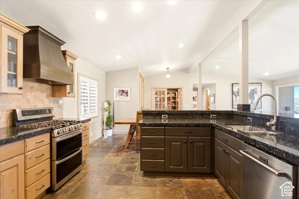 Kitchen featuring custom cabinetry, dark stone countertops, stainless steel appliances, a range hood, and tile flooring