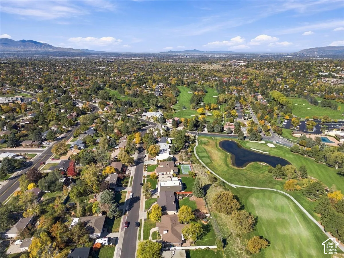 Aerial perspective of a suburban neighborhood featuring extensive green space, a water hazard, manicured grounds, and distant mountain backdrops