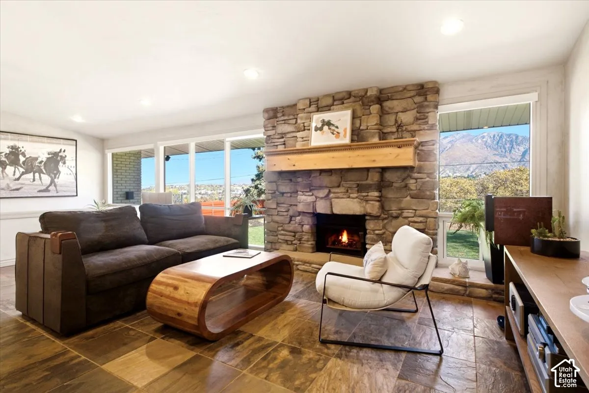 Living area featuring a floor-to-ceiling natural stone fireplace, a prominent wood mantel, large windows, and stone tile flooring