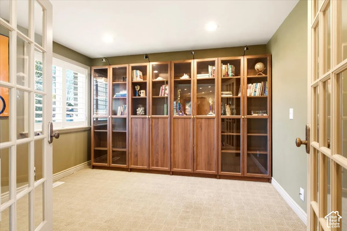 Built-in wood cabinetry with glass-front shelving, integrated cabinet lighting, French doors, and window shutters