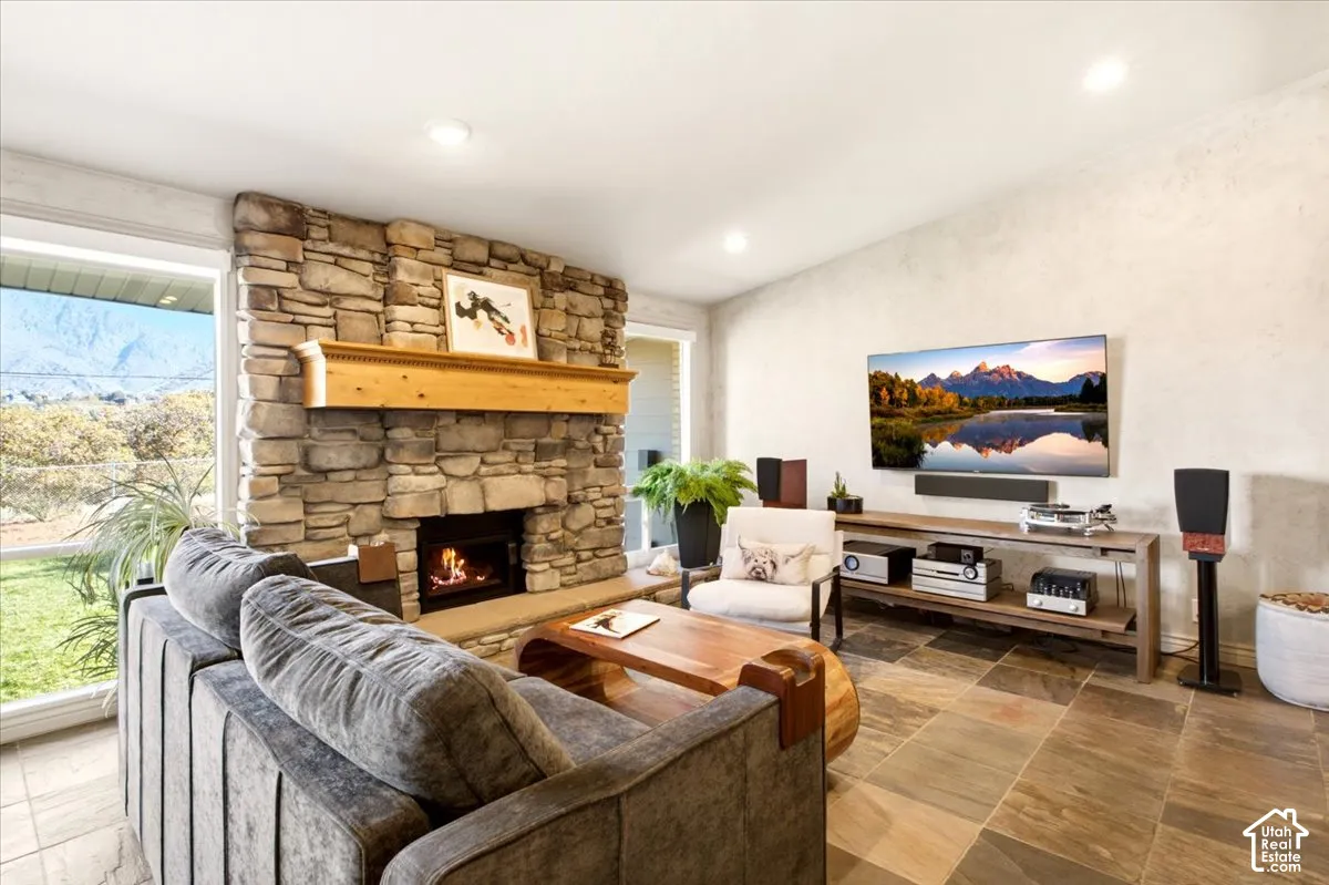 Living area featuring natural stone fireplace surround, custom wooden mantel, tile flooring, recessed lighting, and large windows with mountain scenery