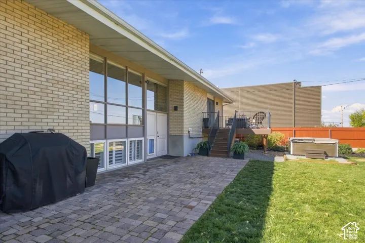 Brick exterior featuring expansive floor-to-ceiling windows, stone paver patio, elevated wood deck with metal railings, and fenced yard