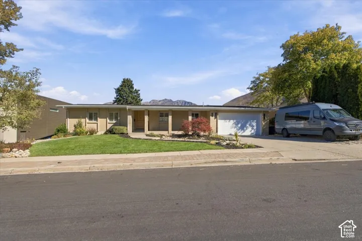 Single-story residence featuring a brick and siding exterior, covered entryway, attached two-car garage, concrete driveway, and mountain backdrop