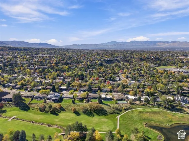 Aerial perspective of an expansive neighborhood featuring mature tree canopy, integrated golf course fairways, a water feature, and distant mountain backdrops