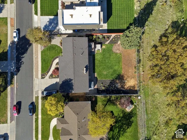 Aerial perspective of a residential property featuring a manicured lawn, paved driveway, concrete walkway, and landscaped garden beds