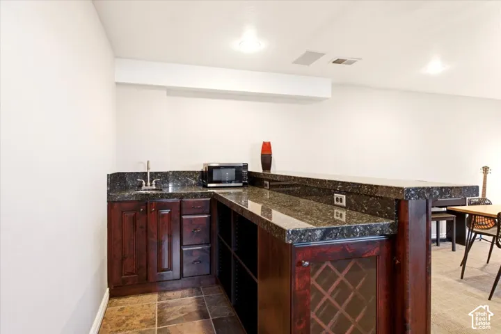 Wet bar featuring dark-toned wood cabinetry, built-in wine rack, stone-finish countertops, and an undermount sink with a gooseneck faucet