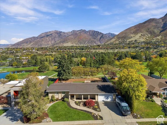 Single-level residence with a concrete driveway, attached garage, covered front porch, and manicured landscaping, set against a mountainous backdrop