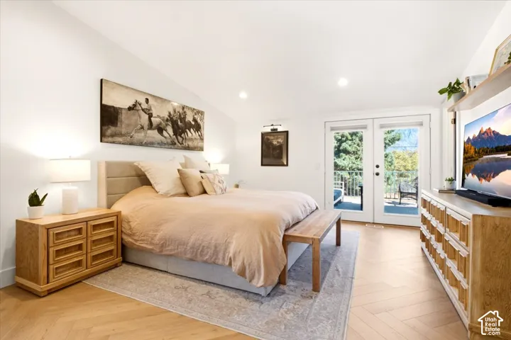 Herringbone-patterned wood-finish flooring, vaulted ceiling with recessed lighting, and double glass-pane doors with outdoor access