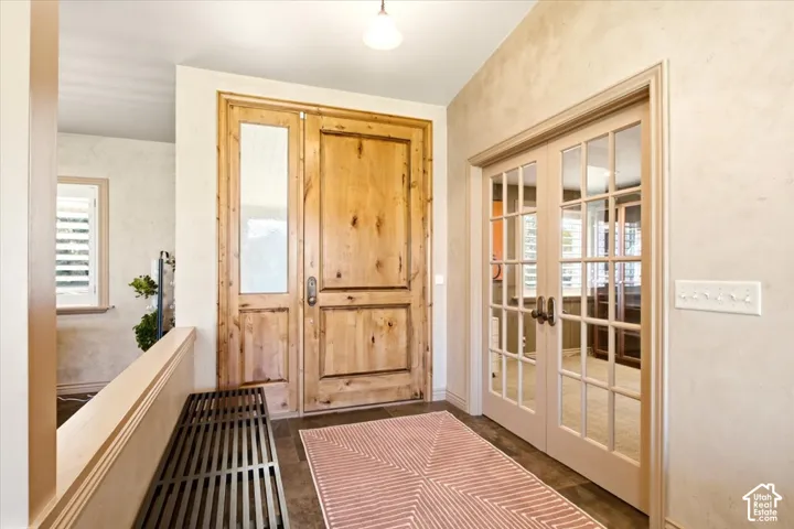 Solid wood entry door with glass sidelight, double French doors with glass panes, textured wall finish, and tile flooring