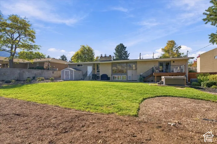 Spacious backyard featuring a manicured lawn, raised wooden deck, detached storage shed, and a hard-plumbed hot tub
