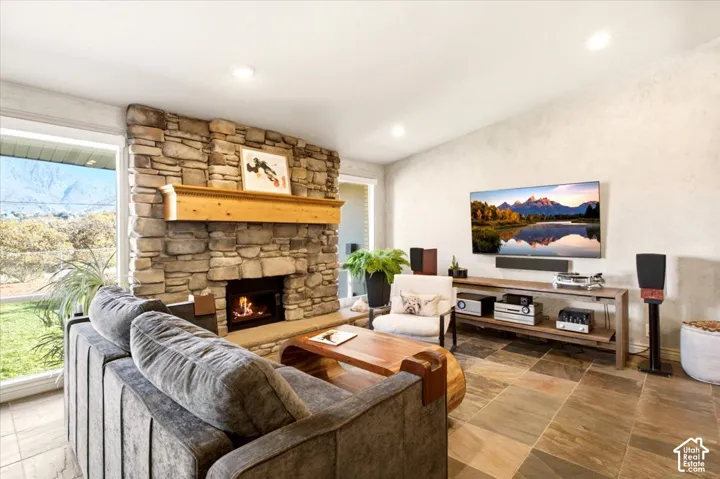 Living area featuring natural stone fireplace surround, custom wooden mantel, tile flooring, recessed lighting, and large windows with mountain scenery