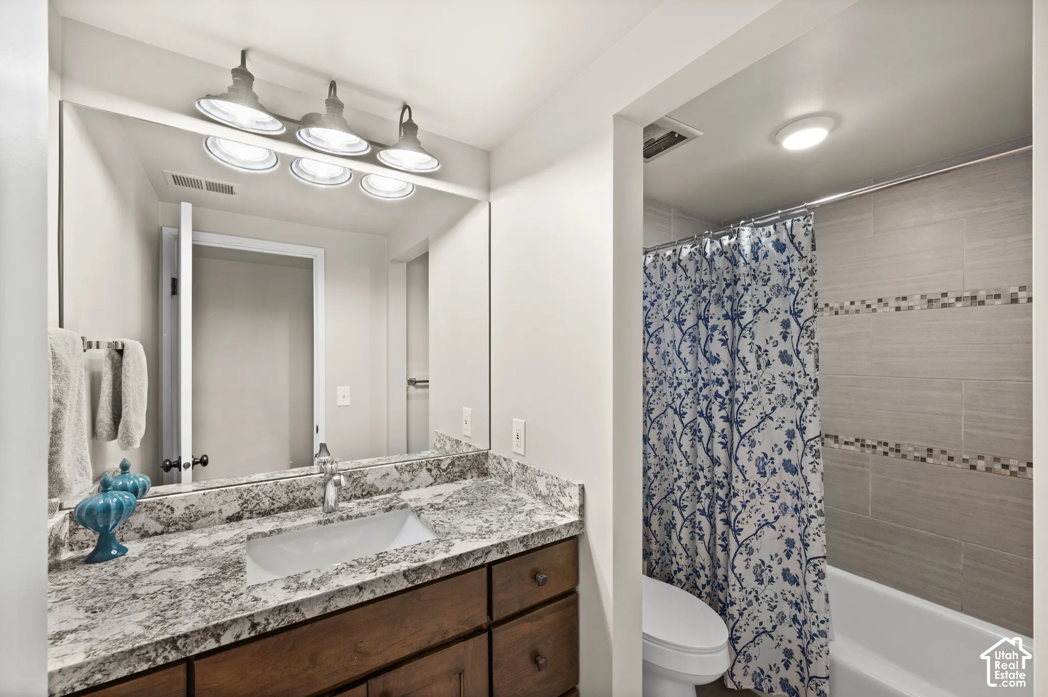 Bathroom vanity with a stone-finish countertop, undermount sink, dark wood-finish cabinetry, and a three-light fixture above a full-width mirror