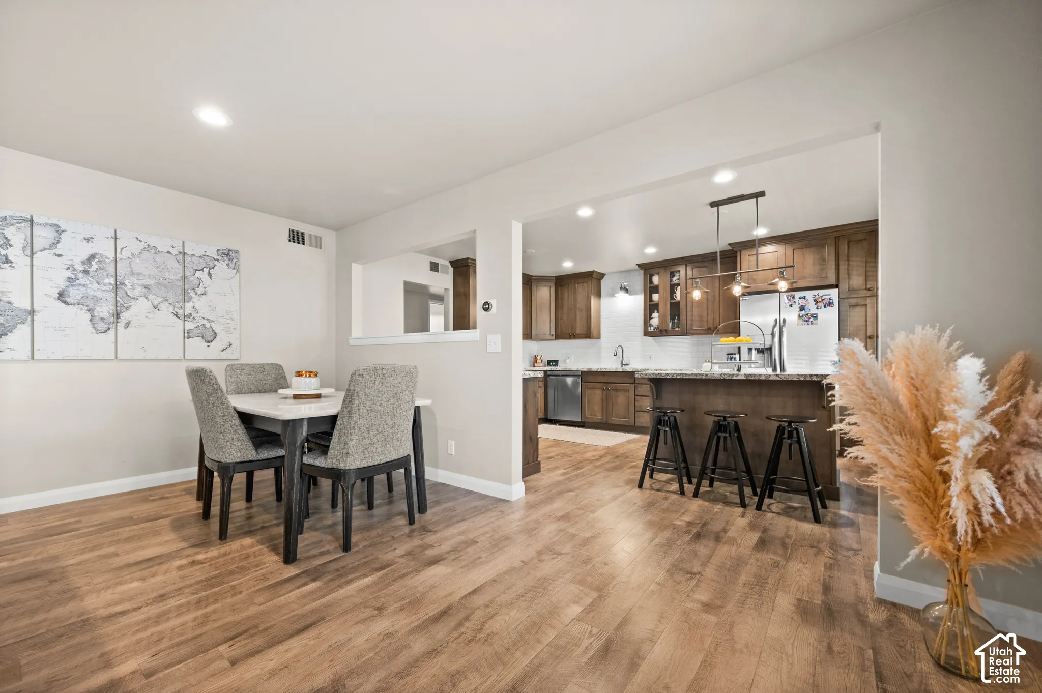 Kitchen featuring wood cabinetry, stone countertops, stainless steel appliances, a tiled backsplash, and an island with overhead pendant lighting, complemented by wood-finish flooring